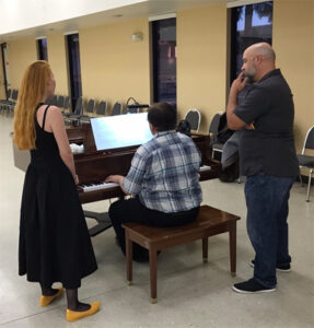 Artistic director and singer looking over the shoulder of a seated paino player.