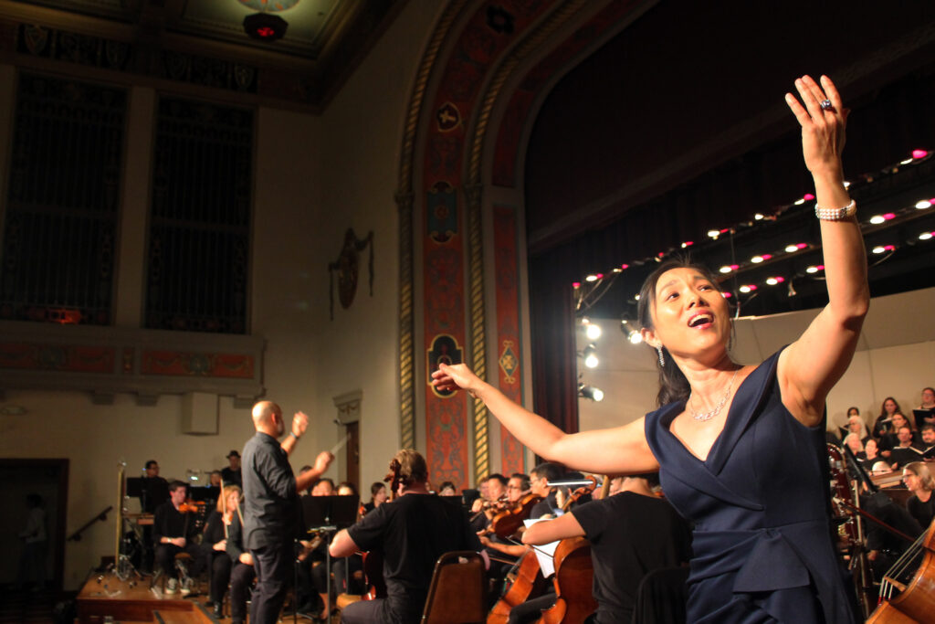 Soprano Grace Lee sings Glitter and Be Gay while Dr. Brian Dehn conducts the orchestra and choir.