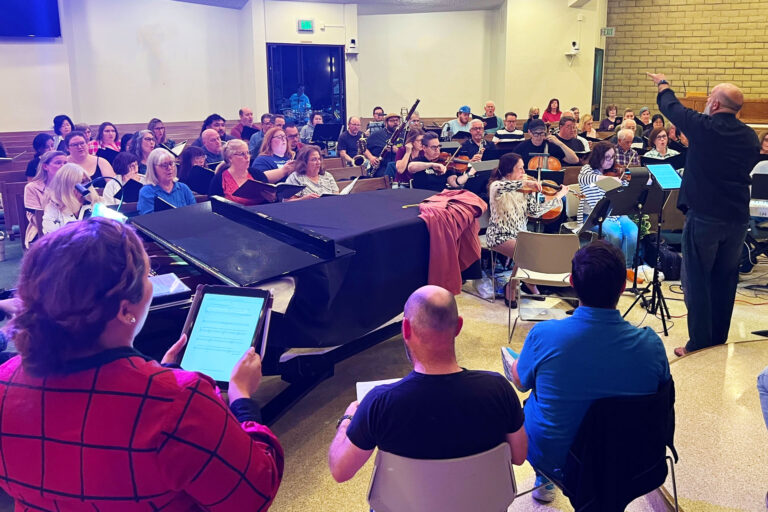 Dr. Brian Dehn standing and conducting the choir and orchestra in a church for rehearsal.
