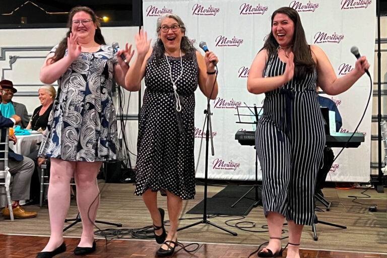 Three women sing in front of microphones.
