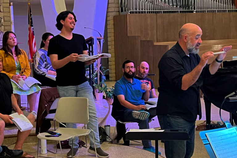 Singer holding music rehearses a solo while Dr. Brian Dehn conducts the orchestra.