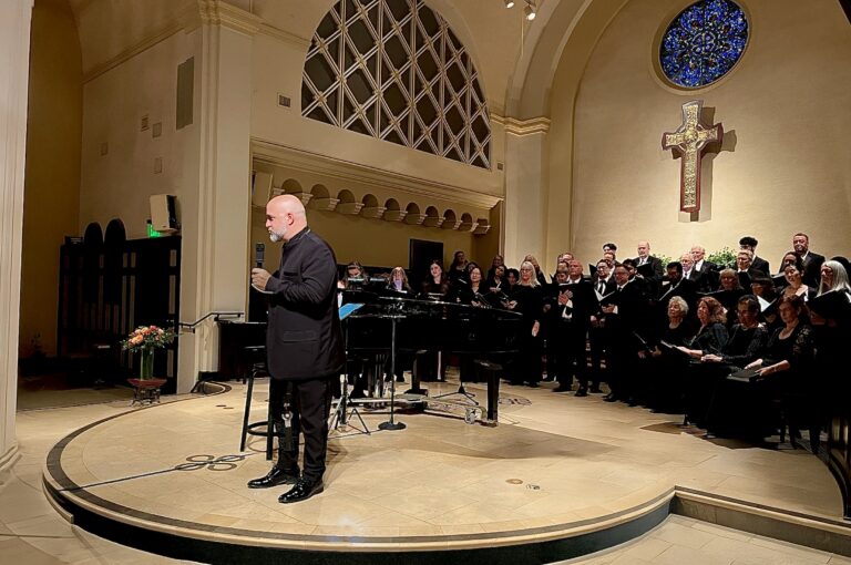 Dr. Brain Dehn standing at the front of the church with a microphone in front of the choir dressed in black.