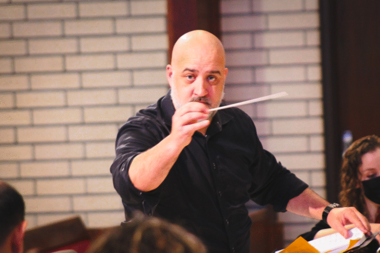 Dr. Brian Dehn in a black shirt against a brick wall background conducting.